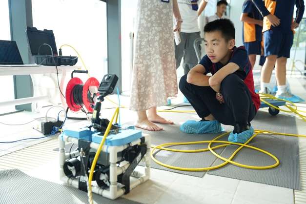 Student adjusting underwater robotics equipment on floor