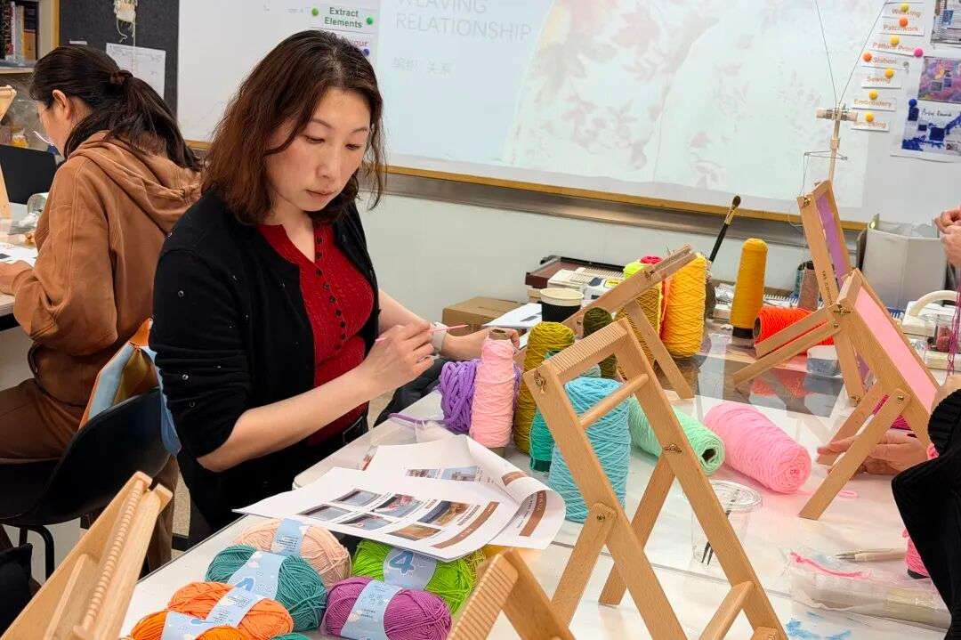 家长在小型梭织机上穿经引纬，近距离体验传统梭织工艺（家校活动）